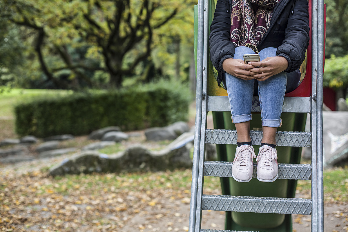 Une fille est assise sur les marches d’un toboggan, tenant fermement son téléphone portable.