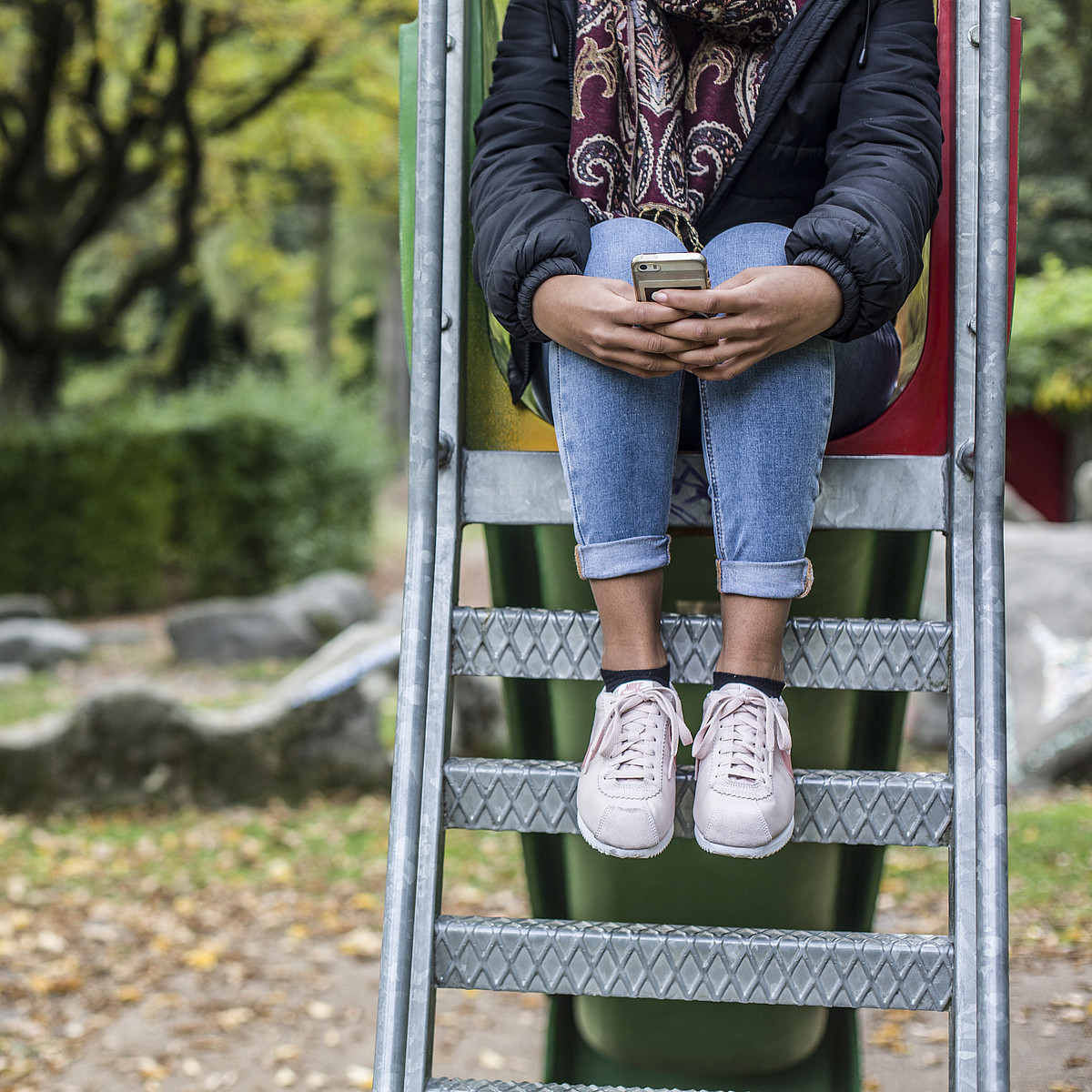 Une adolescente est assise sur l'échelle d'un toboggan. Elle tient fermement son téléphone portable.